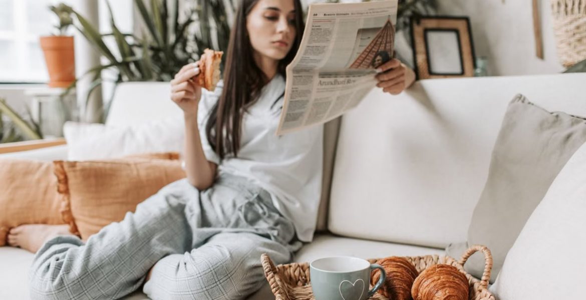 Relaxing morning scene with a woman enjoying coffee and a newspaper on a cozy couch.