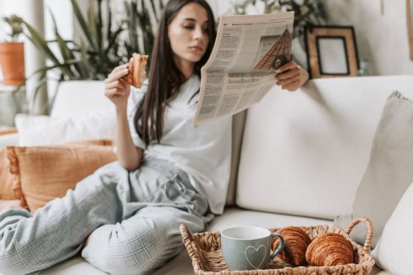 Relaxing morning scene with a woman enjoying coffee and a newspaper on a cozy couch.